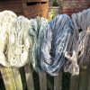 Hanks of wool yarn hanging on a fence showing the range of blue colours