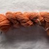 twisted skein of dark salmon pink yarn on a white background