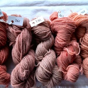 five twisted skeins of yarn ranging in colour from russet red on the left, through red- brown to salmon pinks on the right